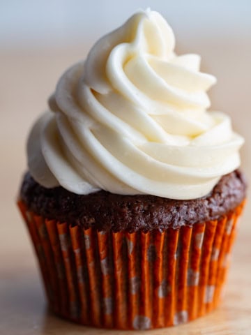 A chocolate cupcake with a large swirl of vanilla frosting in an orange cupcake liner.