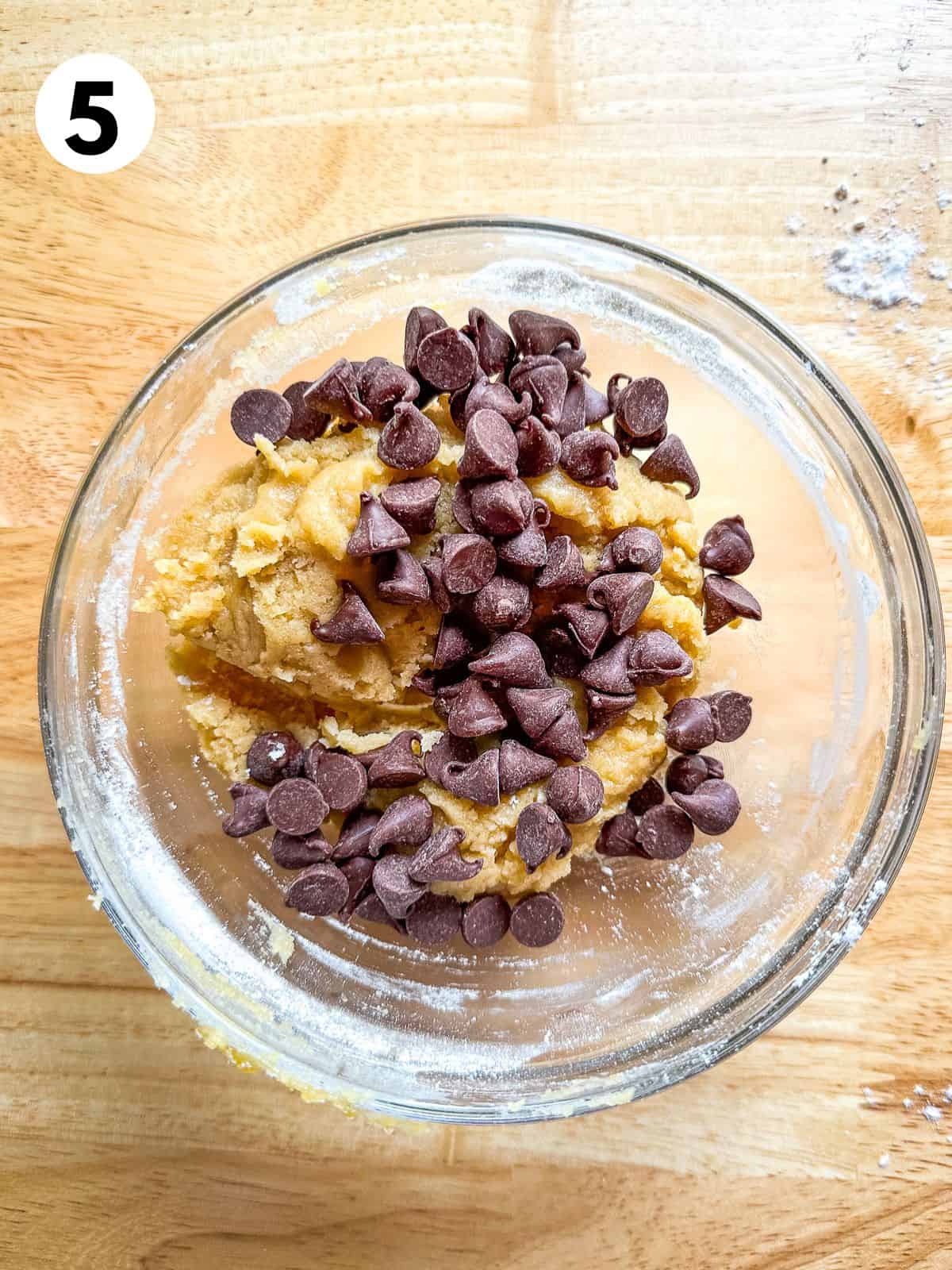 Chocolate chips sprinkled on top of a small batch of chocolate chip cookie dough. The chips are about to be stirred in.