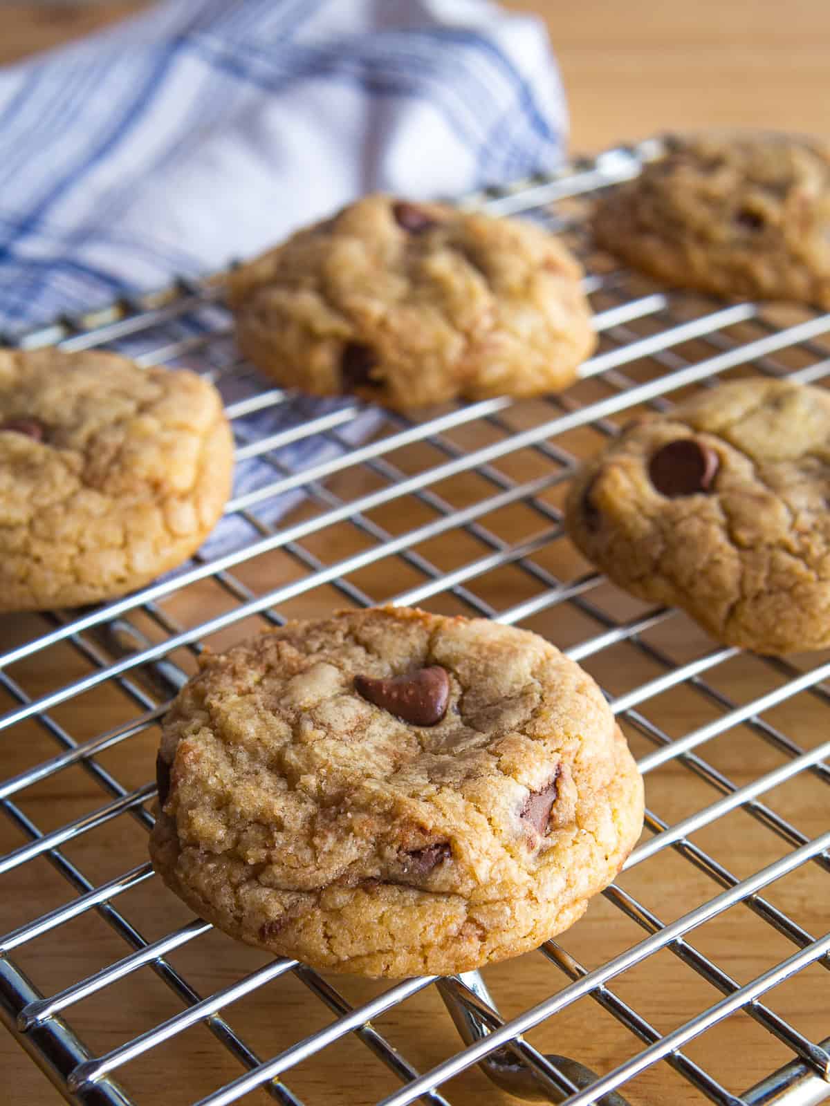 A closeup of a chocolate chip cookie on a wire rack. More cookies are on the rack in the background.