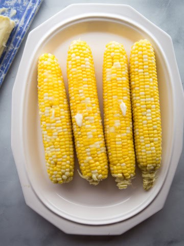 Four ears of boiled corn on a platter.