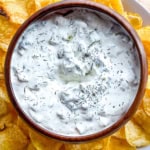 Bowl of dill pickle dip with potato chips surrounding it.