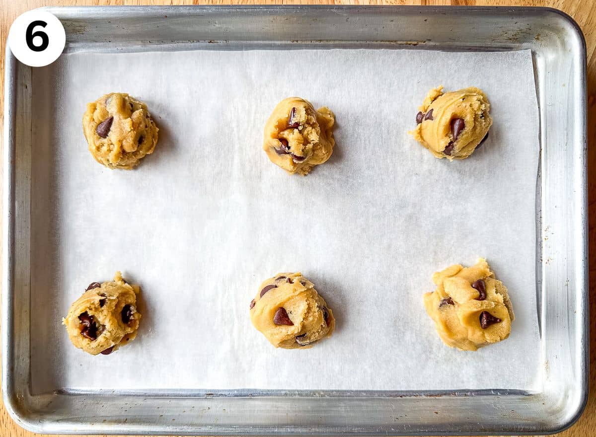 Six scoops of chocolate chip cookie dough on a small baking pan.