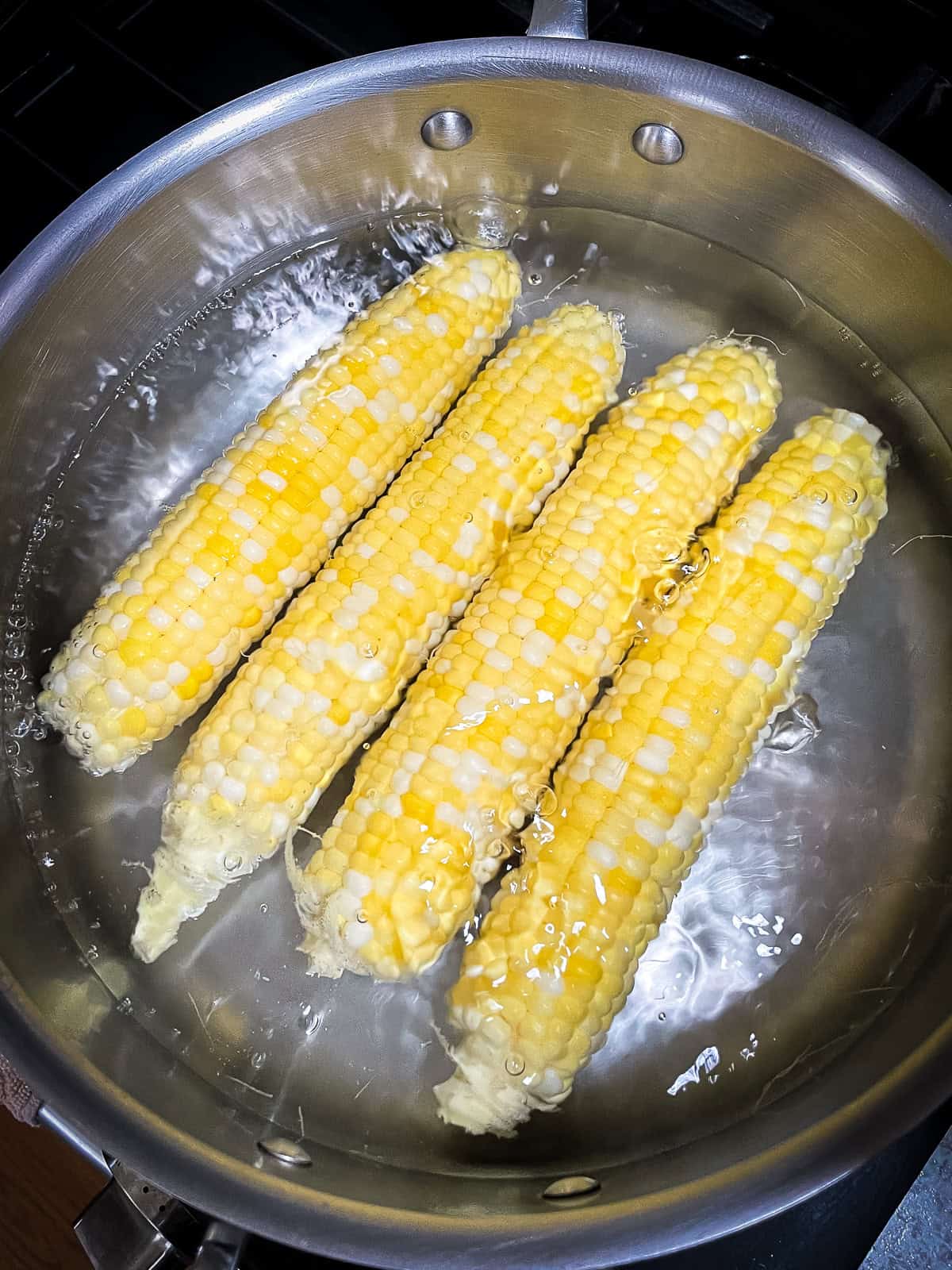 4 stalks of fresh corn boiling in a pot.