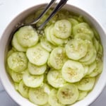 Vinegar cucumber salad in a bowl with two serving spoons.