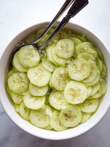 Vinegar cucumber salad in a bowl with two serving spoons.