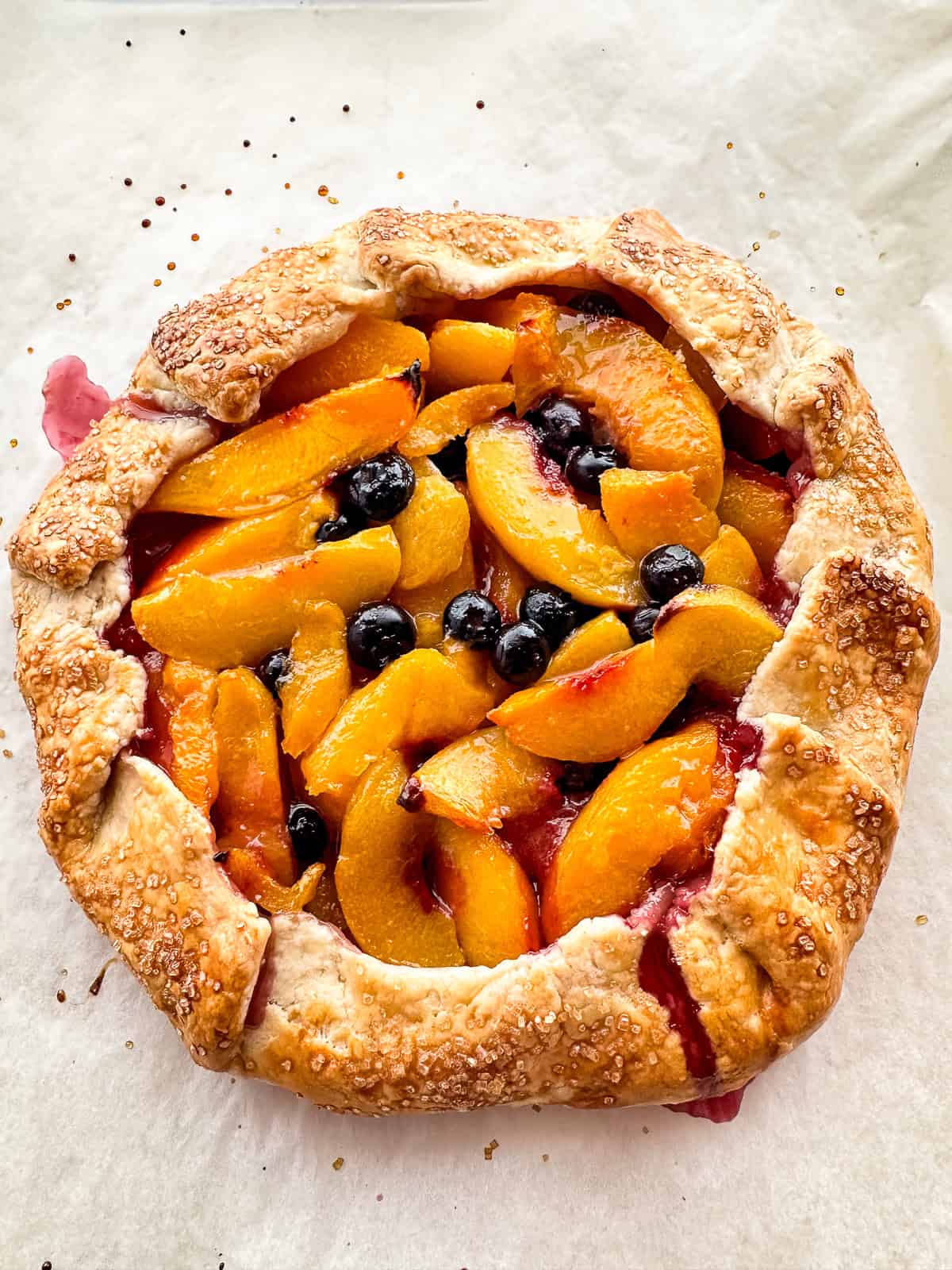 A baked peach-blueberry galette on parchment paper.