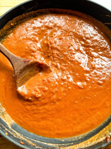 Tomato cream sauce in pan with wooden spoon.