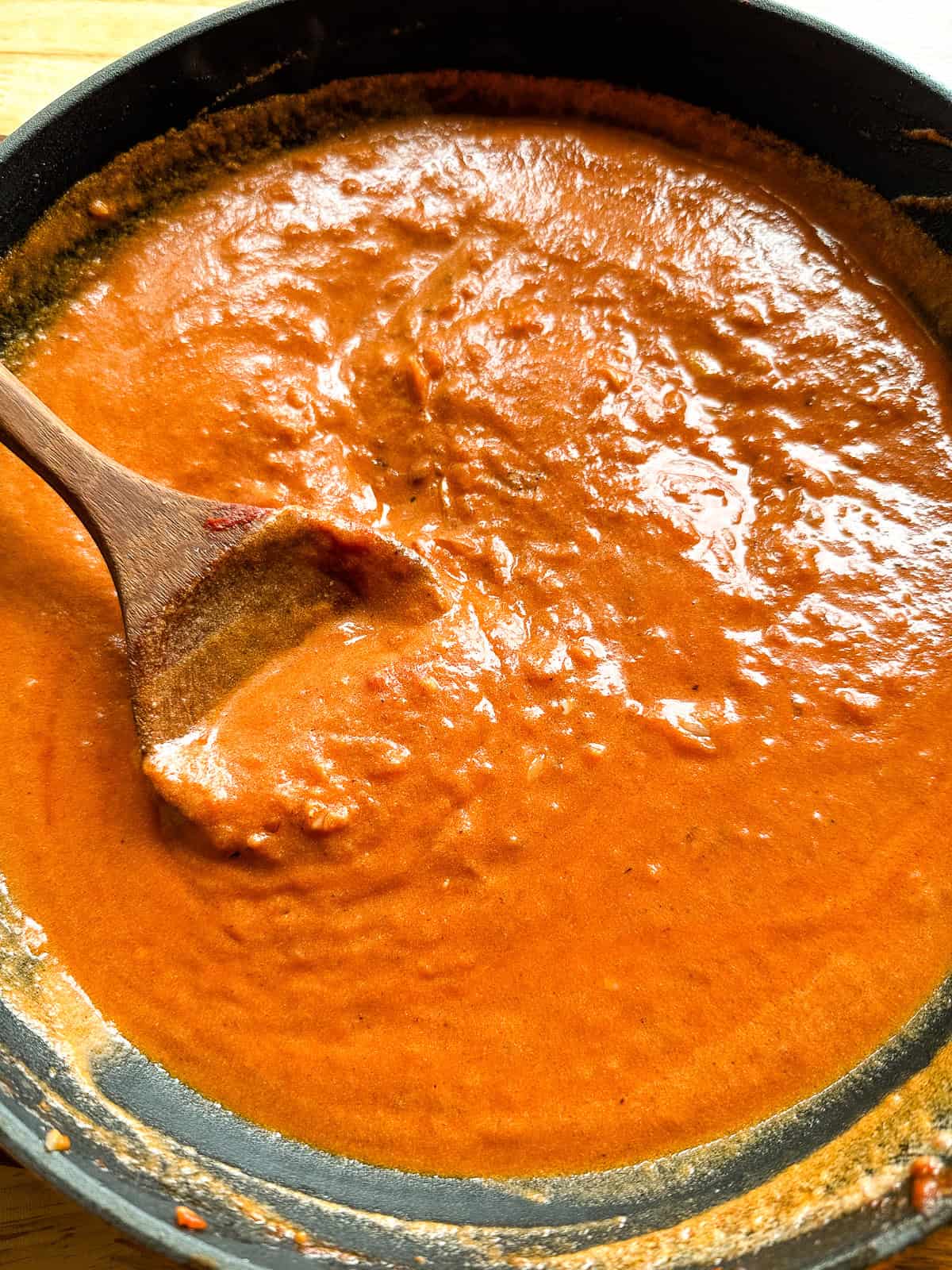 Tomato cream sauce in pan with wooden spoon.