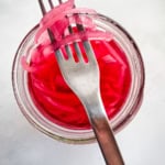 Pickled red onion slices on a fork over a jar of onions.