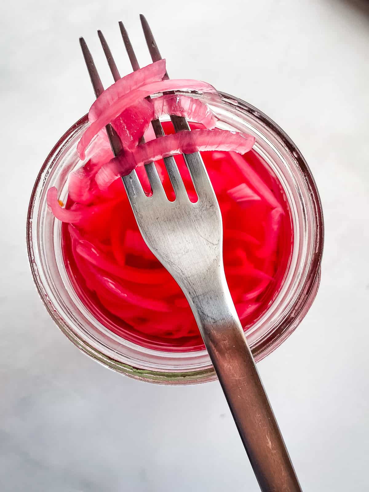 Pickled red onion slices on a fork over a jar of onions.