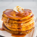 Stack of pumpkin pancakes on a plate with butter and syrup.