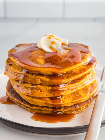 Stack of pumpkin pancakes on a plate with butter and syrup.