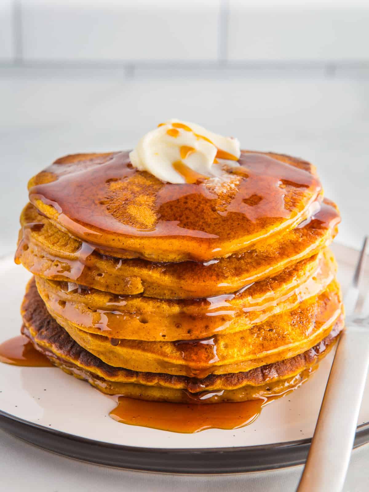 Stack of pumpkin pancakes on a plate with butter and syrup.