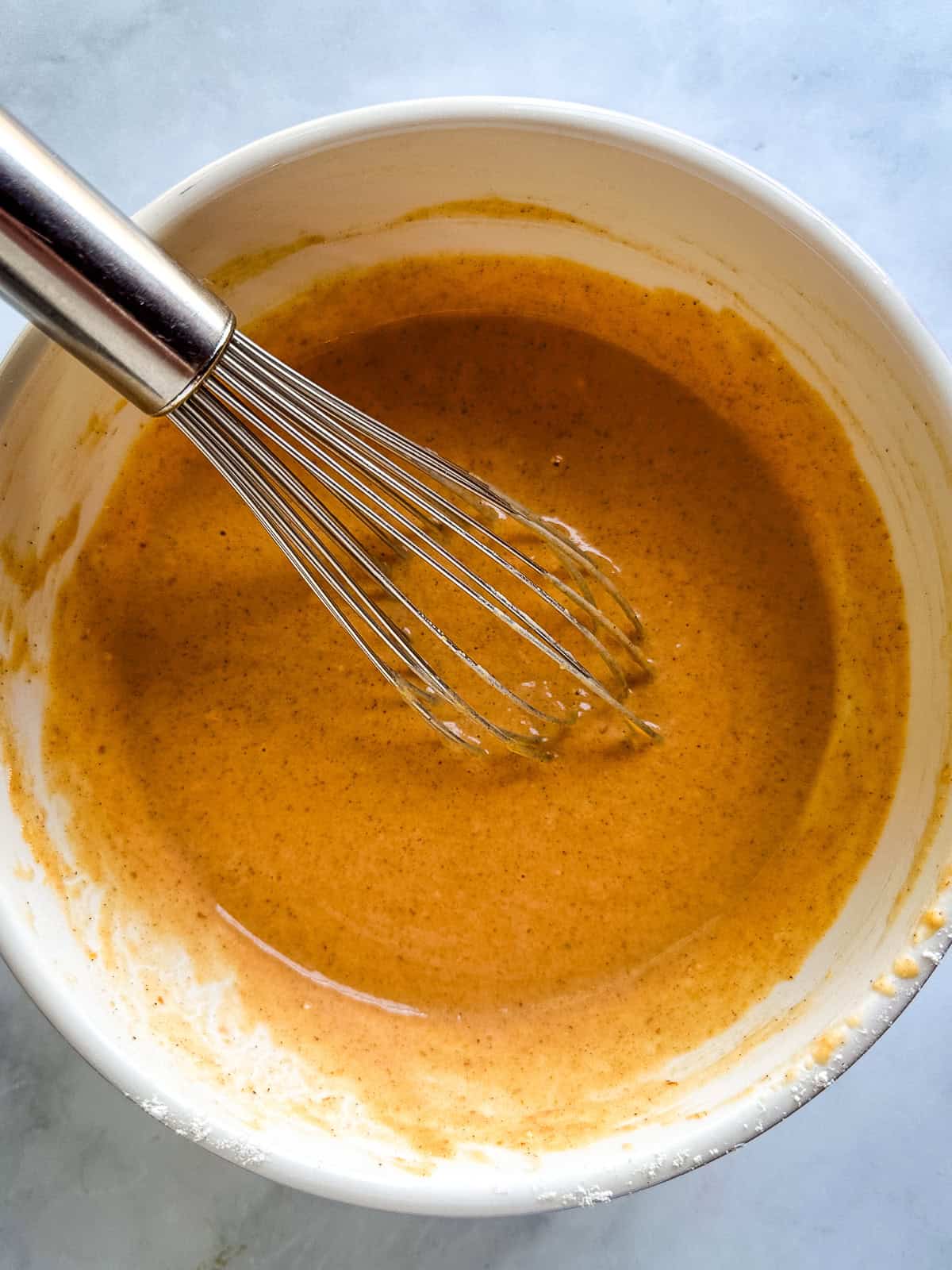 Pumpkin pancake batter in a bowl with a whisk.