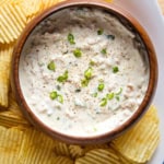 Clam dip in a bowl surrounded by potato chips.