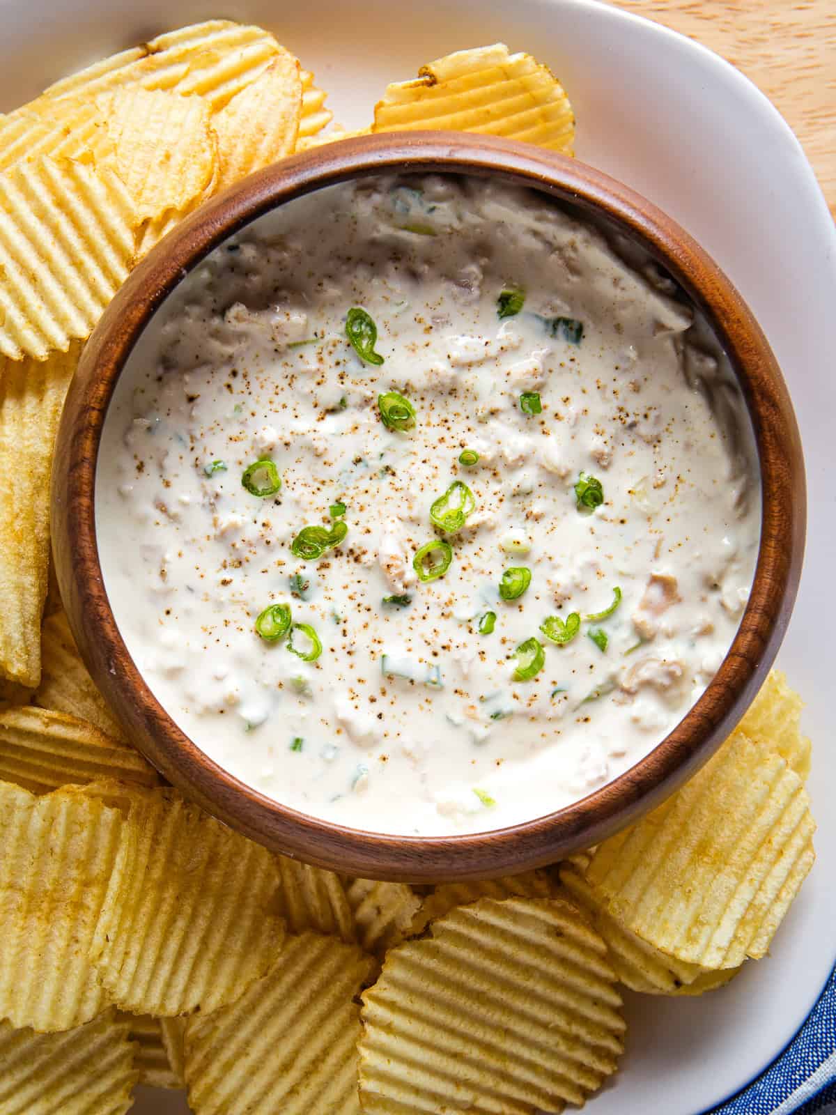 Clam dip in a bowl surrounded by potato chips.