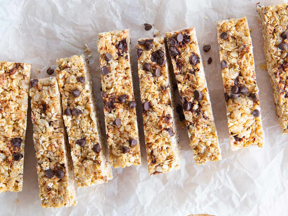 Homemade chewy granola bars, topped with chocolate chips, on a piece of parchment paper.