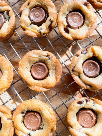 Rolo cookie cups cooling on a wire rack. The top of the cookies are sprinkled very lightly with salt.