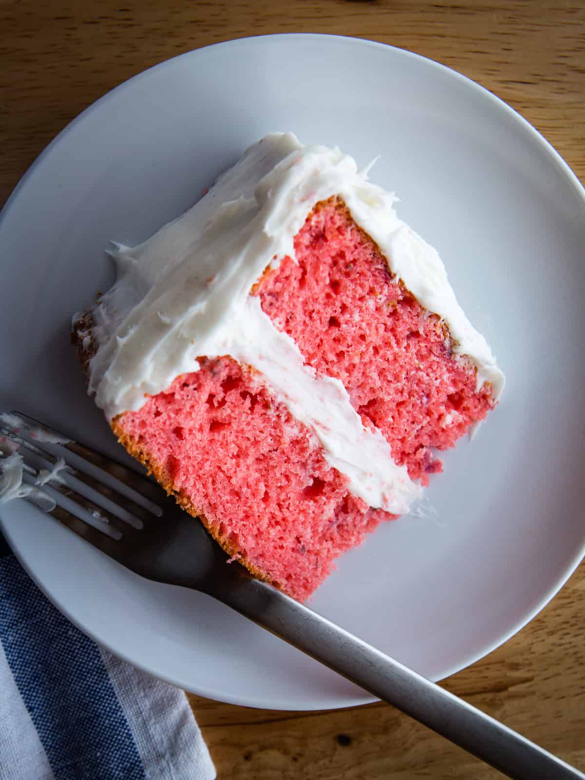 Slice of strawberry cake on a plate frosted with cream cheese frosting.