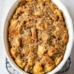 Baked French toast casserole in an oval pan. The casserole is topped with oat streusel topping.