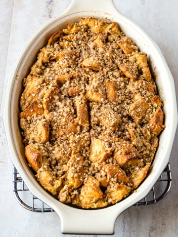 Baked French toast casserole in an oval pan. The casserole is topped with oat streusel topping.