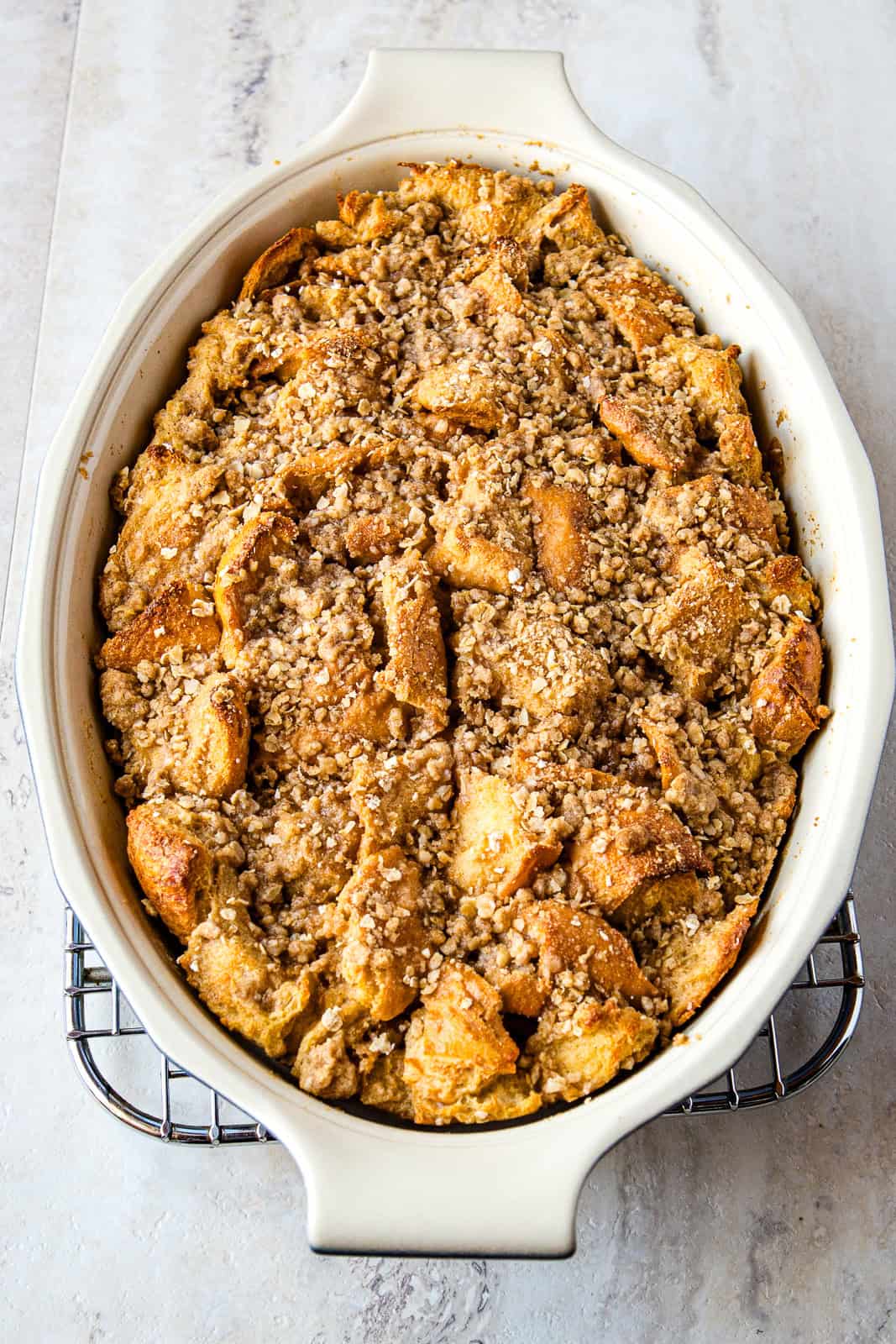 Baked French toast casserole in an oval pan. The casserole is topped with oat streusel topping.