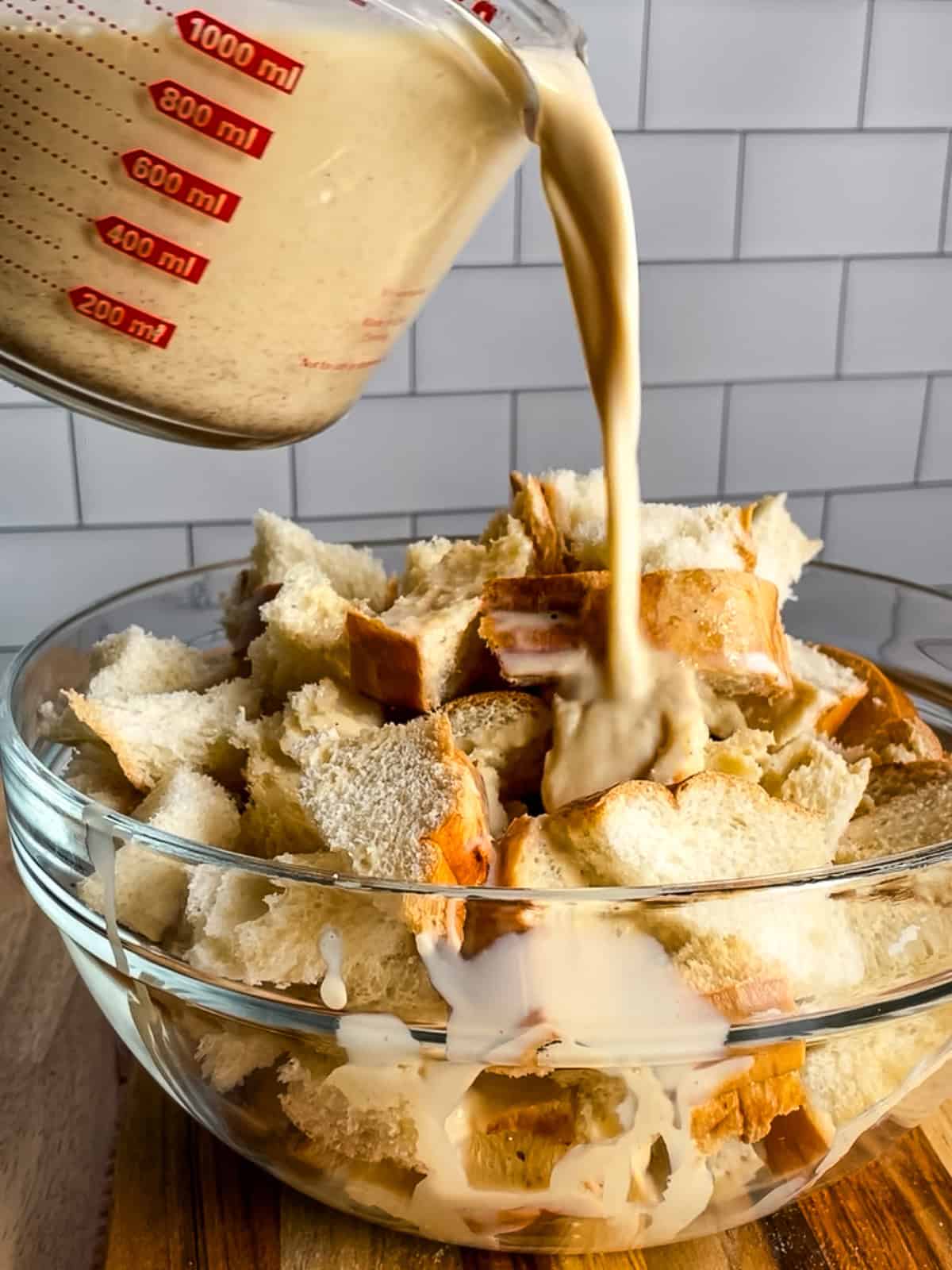Pouring egg custard over pieces of Italian bread for French toast casserole.