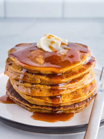 A stack of pumpkin pancakes topped with butter and syrup.