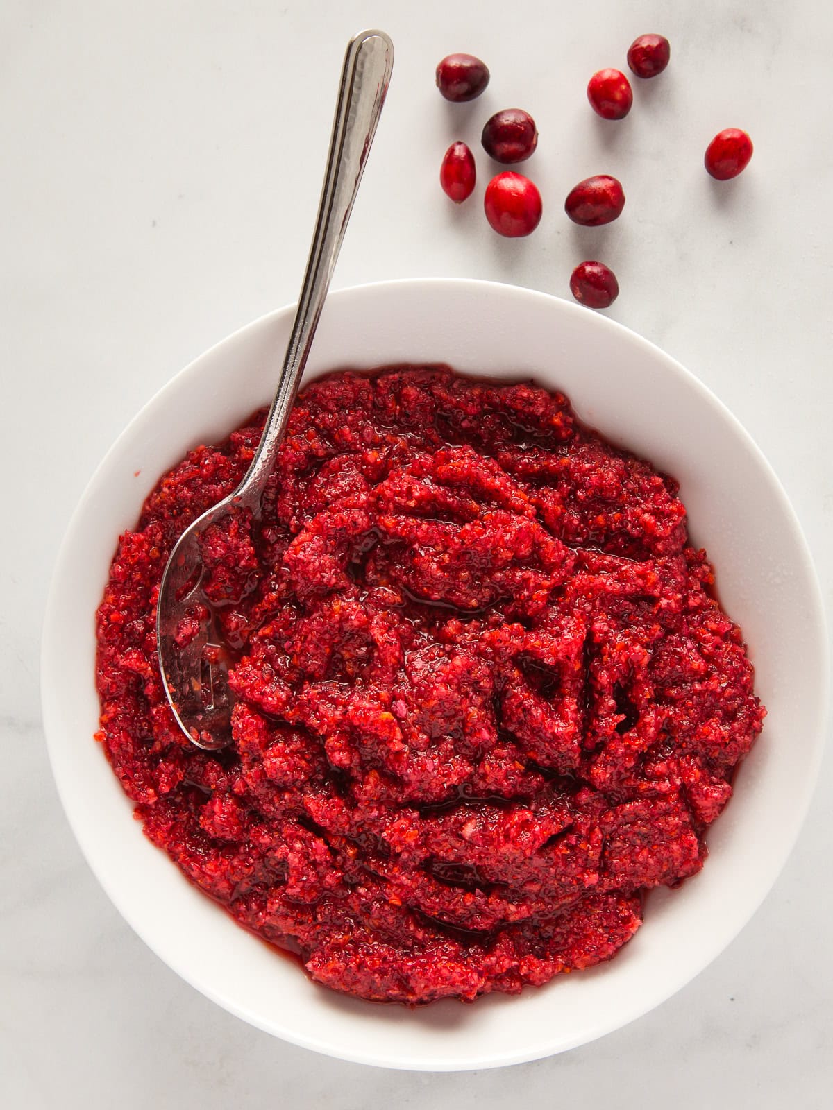 A bowl of cranberry orange relish. A few whole cranberries sit on the counter behind the serving dish.