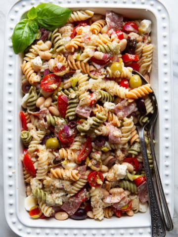 Antipasto pasta salad in a serving dish. A few fresh basil leaves sit in the upper left corner of the dish.