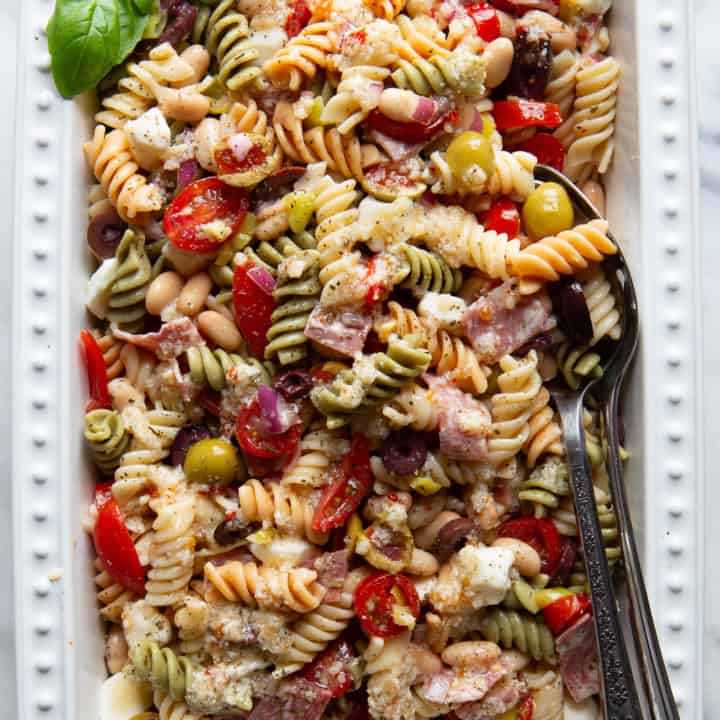 Antipasto pasta salad in a serving dish. A few fresh basil leaves sit in the upper left corner of the dish.